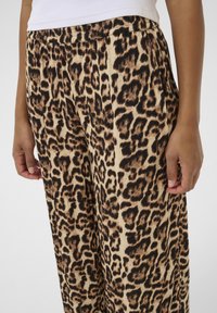 Pantalon imprimé léopard avec une base beige clair, des taches marron foncé et noires, une coupe large et une taille élastique avec des plis.