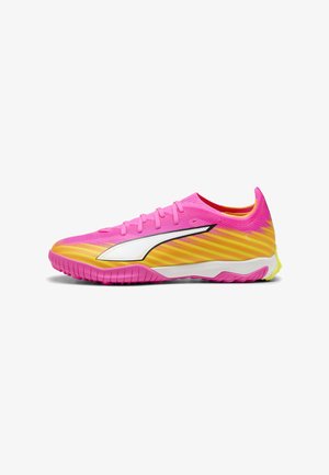 Lavskåret sportssko i pink og gul gradient med hvidt sidelogo, designet til kunstgræs eller indendørs sport med tekstureret sål.