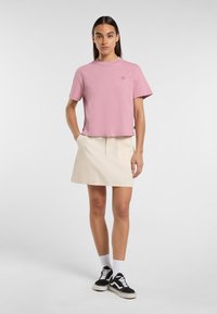 Rosa kortärmad t-shirt med en liten logotyp. Matchas med en krämfärgad kjol och svarta sneakers. Vita ankelsockor.