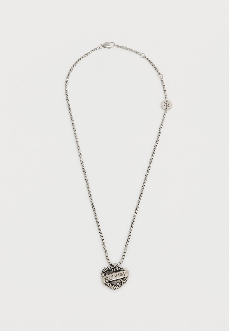 Ασημένιο κολιέ αλυσίδα με μενταγιόν σε σχήμα καρδιάς που διαθέτει μια κορδέλα χαραγμένη με τη φράση "ED HARDY" και ένα μικρό στρογγυλό γούρι κοντά στο κούμπωμα.