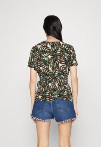 Blusa a maniche corte con un motivo a foglie nere e verdi su uno sfondo chiaro, dettaglio con vita stretta, abbinata a shorts in denim strappati.