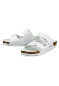 Witte slide sandalen met twee verstelbare banden, een kurken voetbed en een gekartelde rubberen zool, met een eenvoudig en minimalistisch ontwerp.