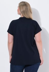 Top corto blu navy a maniche corte realizzato in morbido tessuto, con vestibilità rilassata e orlo leggermente curvo. La vista posteriore non presenta pattern né dettagli.