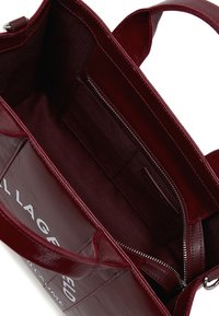 Burgundy leather handbag interior with smooth texture, featuring a zippered pocket and two slip pockets, branded logo visible.