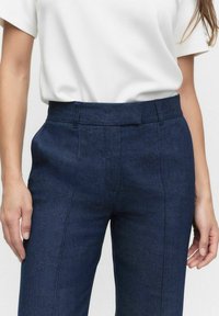 Granatowe spodnie na miarę wykonane z denimu, z wysokim stanem, bocznymi kieszeniami i czystą, klasyczną sylwetką. Gładka faktura z subtelnymi detalami.