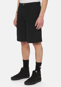 Sort shorts lavet af robuste materialer, med vinkelformede sidelommer og lige snit. Kombineret med sorte høje sneakers og ankelstrømper.