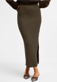 Olivengrön ribbad maxikjol med en sidoöppning, parat med svarta och tan djurmönstrade slip-on-skor. Struktureradtyg, figurnära design.