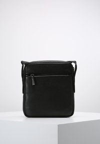 Borsa a tracolla in pelle nera con finitura testurizzata, chiusura con zip, tasca anteriore e tracolla regolabile, caratterizzata da un sottile dettaglio hardware con marchio.
