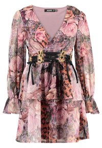 Blommigt mönstrad klänning med långa ärmar, V-ringning, lager av chiffon och ett svart bälte med guldaccenter och snörning. Dominerande färger är rosa och lila.