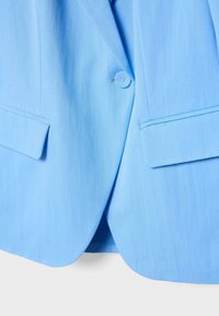 Light blue blazer with a single button closure and two flap pockets on the front, shown from the waist down.
