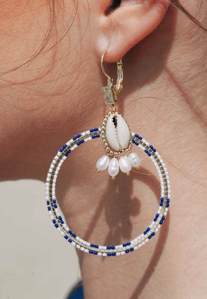 Große Creolen mit weißen Perlen, blauen Akzenten und goldfarbenen Beschlägen. Ein Muschelmittelstück mit Perlenanhängern verleiht Eleganz.