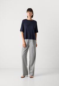 Top blu navy a maniche corte con vestibilità rilassata, abbinato a pantaloni a gamba larga grigio chiaro a righe sottili e sandali con tacco marroni.