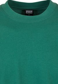 Camiseta verde de algodón suave, con cuello redondo y etiquetada como "URBAN CLASSICS" en tamaño mediano en la etiqueta interior.