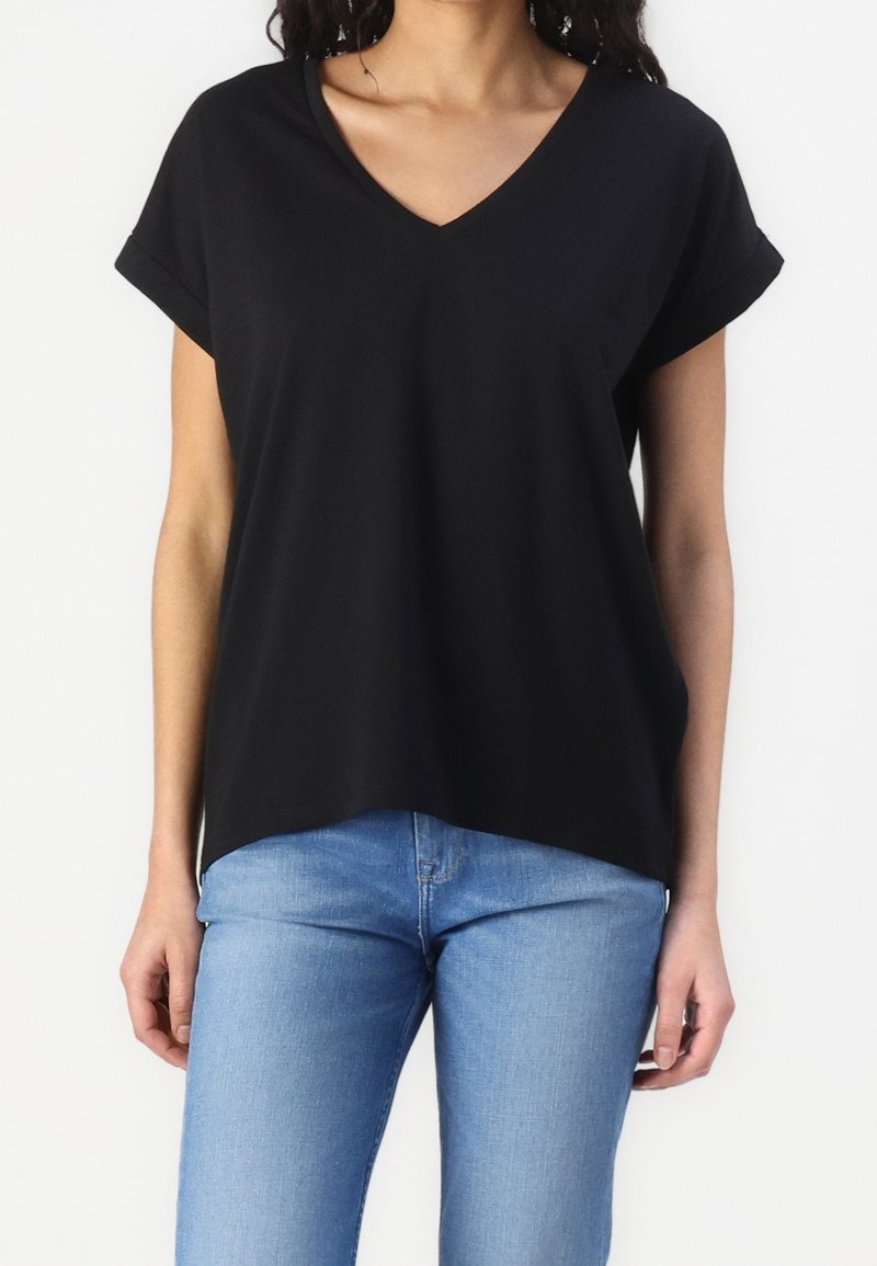 T-shirt noir à col en V avec des manches courtes roulées, présentant une coupe décontractée et un tissu doux. Associé à un jean skinny bleu clair.