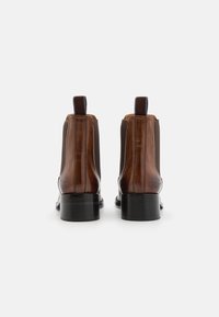Bottines en cuir marron avec des panneaux latéraux élastiques, talon noir plat et tirette. Texture lisse avec des détails de couture discrets.
