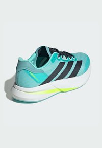 Baskets de sport turquoise avec trois rayures noires, tige texturée, semelle intermédiaire Lightstrike avec accent jaune, col rembourré et fermeture à lacets.
