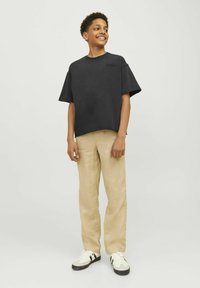 Svart, kortärmad oversized t-shirt med rund halsringning, tillsammans med beigefärgade, löst sittande byxor och vita sneakers med svarta accenter.
