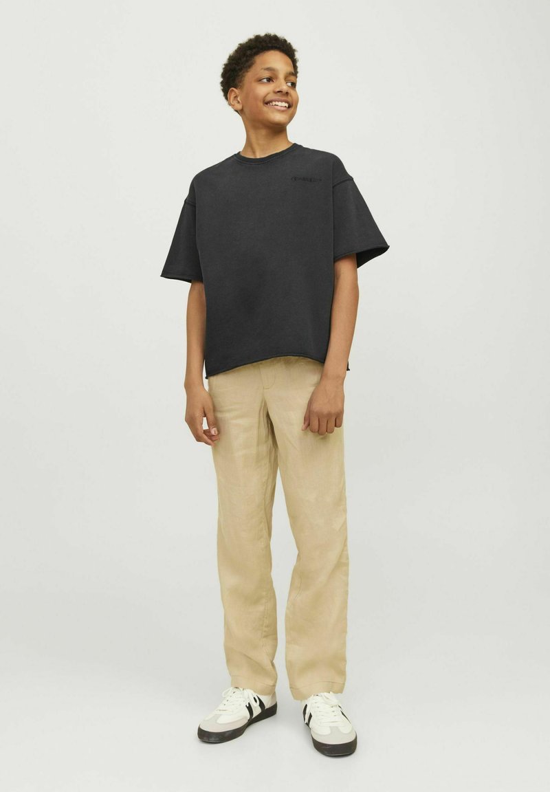 Svart, kortärmad oversized t-shirt med rund halsringning, tillsammans med beigefärgade, löst sittande byxor och vita sneakers med svarta accenter.