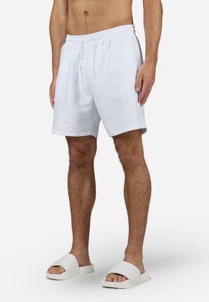 Hvite stripete badebukser med elastisk liv og snor, med en avslappet passform. Brukt med hvite åpne sandaler.