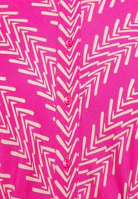 Pink button-up shirt featuring a zigzag pattern in white. It has pink buttons and a smooth, lightweight fabric texture.