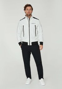 Vitt jacka med svarta detaljer, dragkedjefickor och ribbade ärmar. Kombineras med svarta byxor och vita sneakers för en koordinerad look.