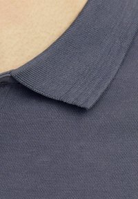 Šedý límeček polo trička s hladkou texturou, nabízející krátký, zkroucený design a jemný pletený vzor.