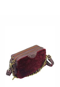 Sac à bandoulière bordeaux avec une texture pelucheuse, des accents en cuir, deux zips dorés et une chaîne métallique. Forme rectangulaire, design compact.