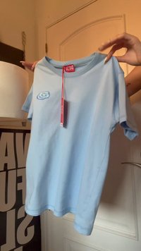 Άτομο κρατά ένα ανοιχτό μπλε t-shirt της Diesel με μικρό λογότυπο στο στήθος και μια κόκκινη ετικέτα μάρκας που κρέμεται από τον γιακά.