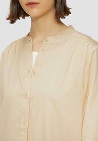 Beige knoopshirt met ronde halslijn, van zachte katoenstof, subtiele textuur en geplooide details op de schouders.