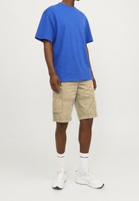 T-shirt di cotone blu, maniche corte, vestibilità comoda; pantaloni cargo beige con diverse tasche; sneakers bianche; calze bianche con testo nero.