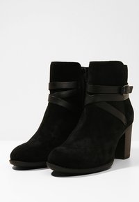 Mustat mokkanahkaiset nilkkurit pyöreällä kärjellä, paksulla korolla ja kahdella mustalla nahkahihnalla, joissa on solkiviviste. Sivussa vetoketju.