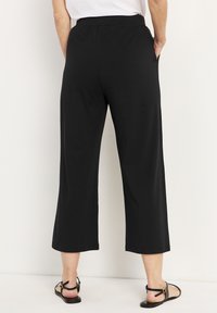 Svarta, löst sittande cropped byxor med elastisk midja och sidofickor, gjorda av mjukt tyg. Bärs med svarta sandaler.