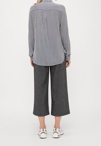 Camicia a righe a maniche lunghe con colletto button-down, abbinata a pantaloni larghi grigi e sneaker bianche. Presenta un delicato design del retro.