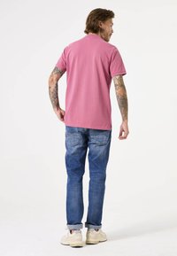 Camiseta de algodón rosa de manga corta, con detalle de abertura en la espalda, combinada con jeans de denim azul con acabado desgastado y puños enrollados.