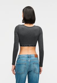 Γκρι κοντό τοπ με μακριά μανίκια και μαύρη λωρίδα με λογότυπο. Φορεμένο με μπλε τζιν ψηλόμεσο, με δερμάτινη ετικέτα και πίσω τσέπες.