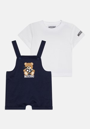 Hvit t-skjorte med kort erme og logo på ermet, kombinert med marineblå arbeidsbukser med et teddy-bear motiv og justerbare stropper.
