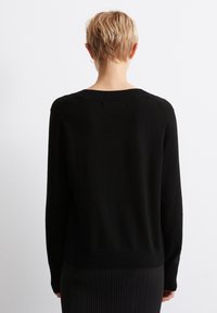 Svart strikket genser med ribbestrikket kant og mansjetter, med avslappet passform og enkelt design, sett bakfra.