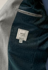 Szary żakiet z teksturowanym materiałem zewnętrznym. Ciemnoniebieskie wnętrze z geometrycznym wzorem i metką z napisem "NEXT TAILORING REGULAR FIT".
