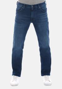Vaqueros de denim azul oscuro con un diseño de pierna recta, estilo de cinco bolsillos, parte frontal desgastada y cierre de botón de metal, combinados con zapatillas blancas.