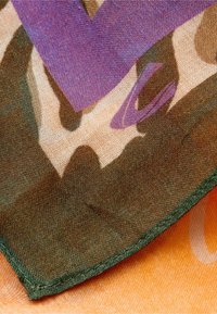 Wielokolorowy szalik z wzorem kamuflażu w fioletowych akcentach. Wykonany z lekkiego materiału, ma zielony stębnowany brzeg.