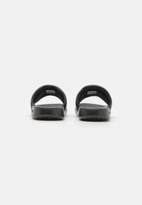 Infradito neri con retro aperto, superiore a texture morbida e suola rigata per una maggiore aderenza. Presenta un branding minimale sul lato.