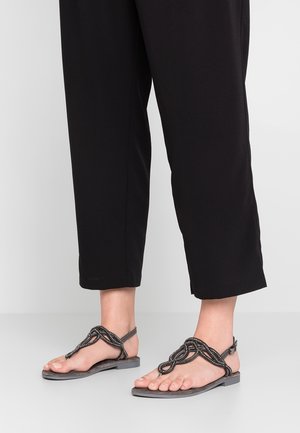 Zwarte platte sandalen hebben een gevlochten bandontwerp met kralenaccenten, een platte zool en een open teen stijl, gecombineerd met zwarte cropped broek.
