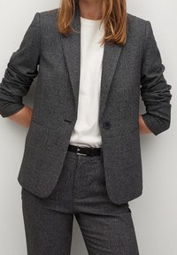 Szary blezer w kratę z pojedynczym guzikiem, klapami typu notch i dwoma przednimi kieszeniami, zestawiony z białym T-shirtem i czarnym paskiem.