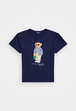 Mornarska bombažna majica s vezenim medvedom, ki nosi črtast outfit, sončna očala in drži zeleno kapo. Klasična zasnova s krožnim ovratnikom.
