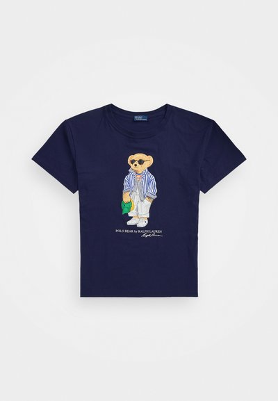 Ναυτικό βαμβακερό t-shirt με κεντητό αρκούδο που φορά ριγέ ρούχο, γυαλιά ηλίου και κρατάει ένα πράσινο καπάκι. Κλασικός σχεδιασμός με στρογγυλή λαιμόκοψη.