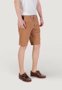 Shorts en coton marron avec une coupe droite, dotés d'une fermeture à bouton et de poches latérales, associés à des chaussures bateau en cuir marron.