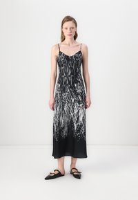 Zwart-witte zijden jurk met een vloeiende silhouet. Het heeft dunne bandjes, een diepe V-hals en een dynamische, veerachtige print. Platte zwarte schoenen.