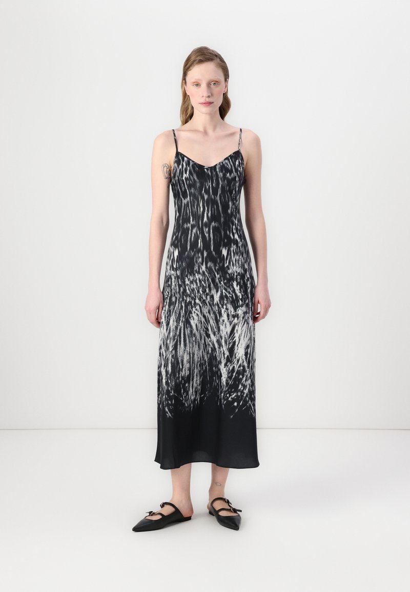 Zwart-witte zijden jurk met een vloeiende silhouet. Het heeft dunne bandjes, een diepe V-hals en een dynamische, veerachtige print. Platte zwarte schoenen.