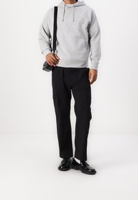 Grå huvtröja med en framficka, ihop med svarta cargo-byxor med sidofickor och svarta slipskor.