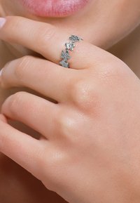 L'anello floreale in argento presenta diverse piccole decorazioni a forma di fiore disposte lungo una delicata fascia, evidenziando dettagli intricati e una superficie liscia.